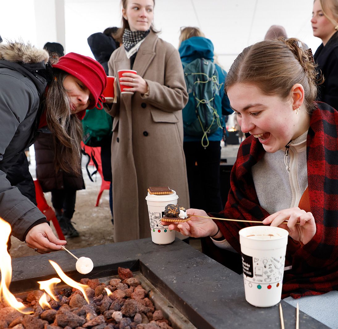 Étudiante qui fait griller une guimauve sur un feu de foyer dans une ambiance festive